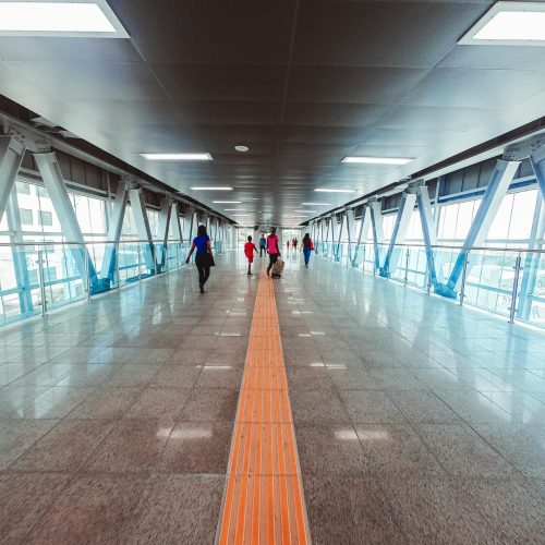 A bright, modern pedestrian walkway in an urban transportation terminal, featuring people walking.