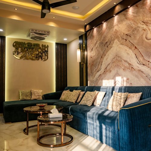 Elegant living room with blue sofas, marble wall, and modern lighting creating a warm ambiance.